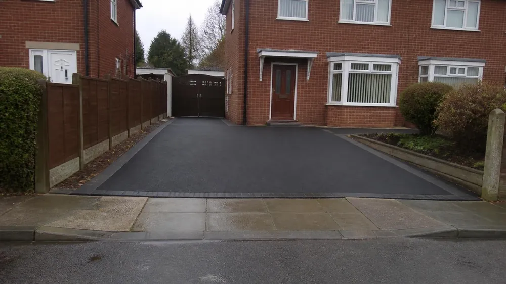 Example image: smooth black tarmac driveway with block edging beside a 1960s semi